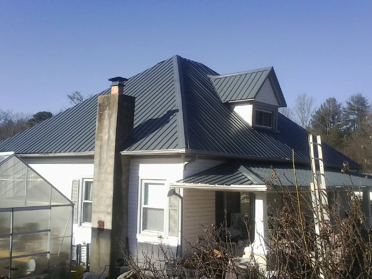 Dark blue standing seam metal roof on a white farmhouse with dormer — Slate & Tile Roof Repair by Roofing Brothers in Wolcottville