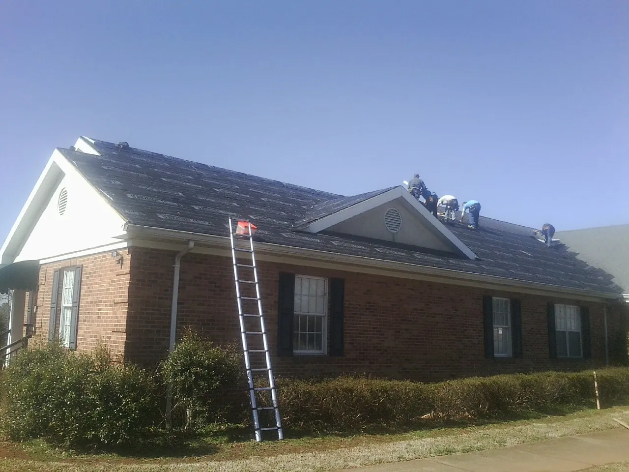 Crew tearing shingles off a brick ranch roof with a ladder set — Emergency Roof Repair work by our crew in Wolcottville