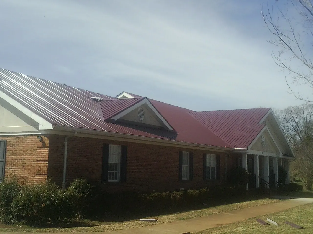 Red metal roof with gabled entries on a long brick building, from a Hail Damage Roof Repair job in Wolcottville
