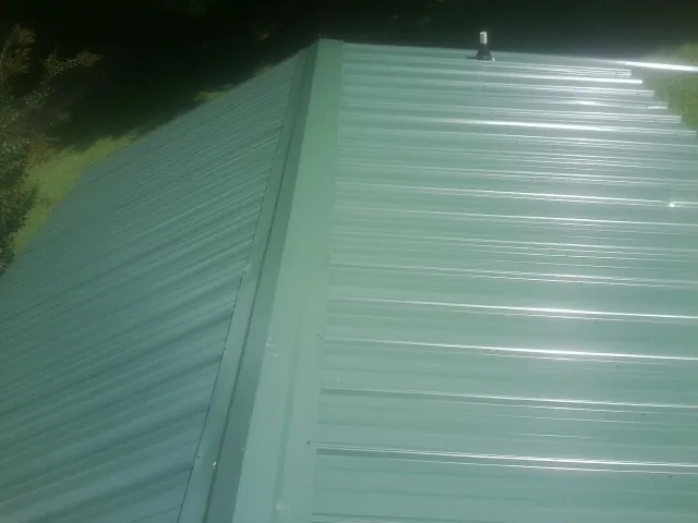 New green metal panels meeting at the ridge of a roof — Flat Roof Repair work by our crew in Wolcottville