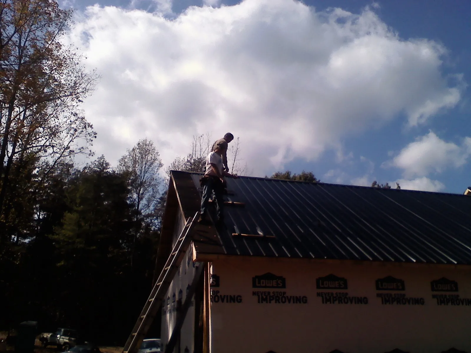 Roofer fastening dark metal panels high against a cloudy sky, from a Roof Inspection job in Wolcottville