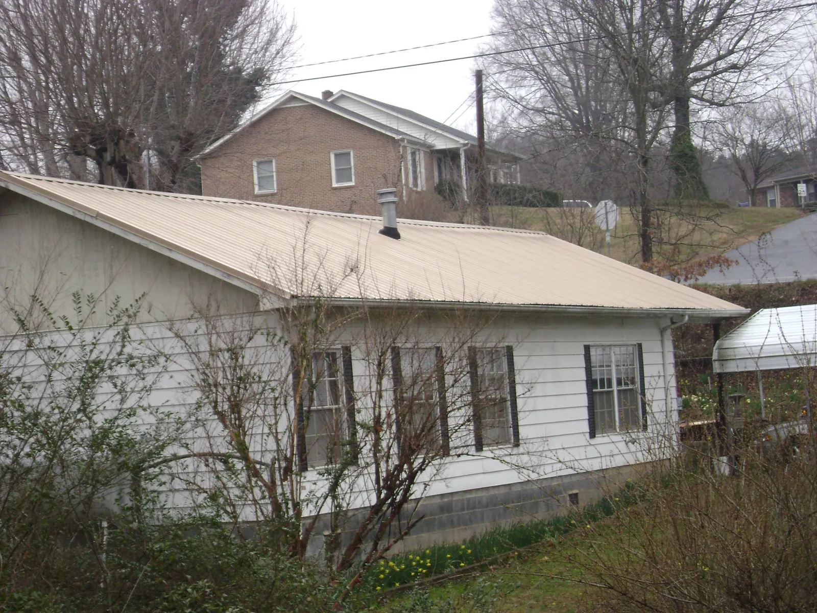 Tan metal roof on a white sided house set into a hillside — Commercial Roofing by Roofing Brothers in Wolcottville